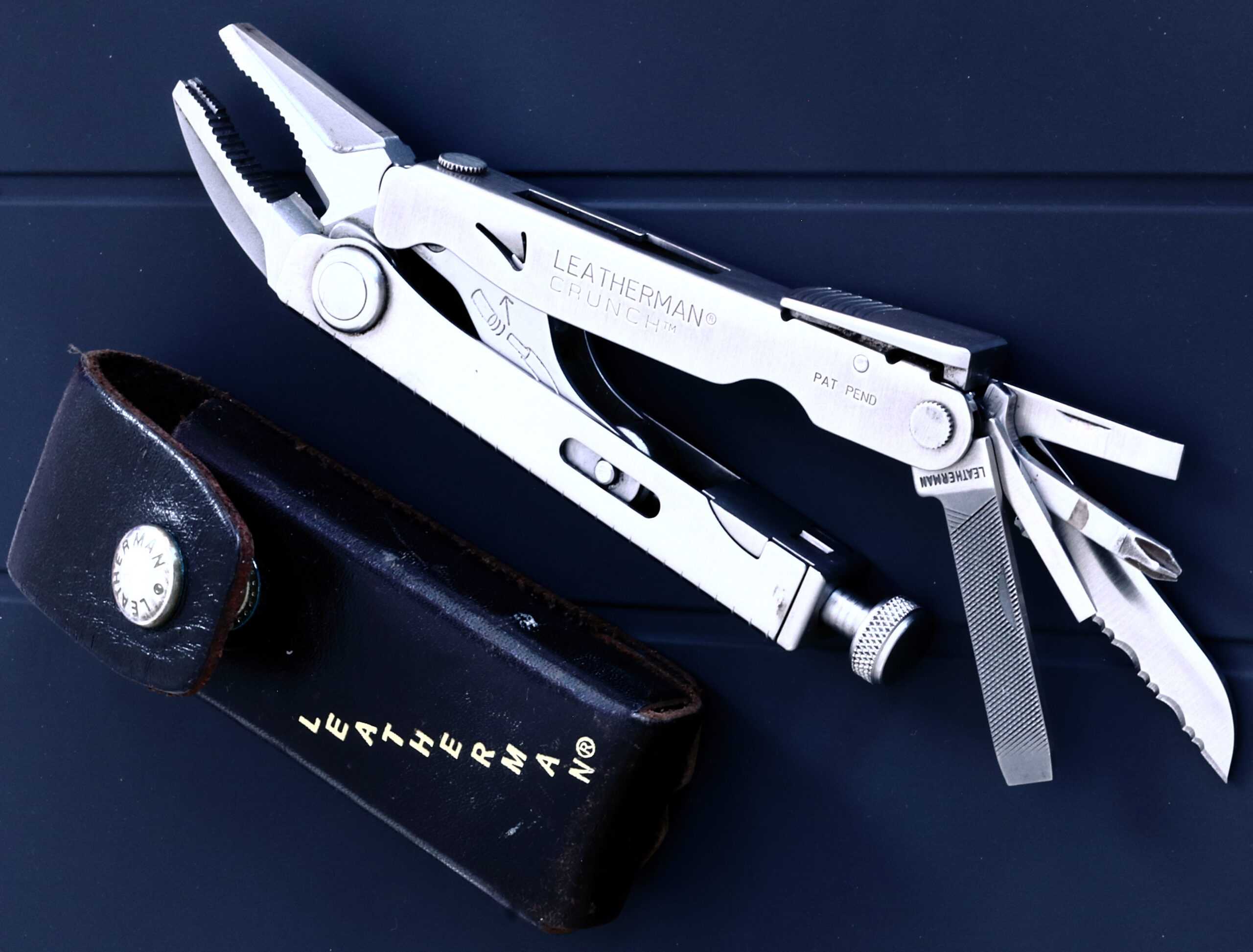 Leatherman Crunch locking-plier multi-tool opened beside its leather sheath